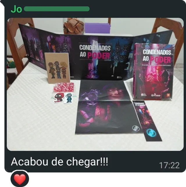 Mensagem com a foto do livro, do escudo do mestre aberto, de um pôster, dos dados, dos adesivos e do marcador sobre a mesa, e o texto: "Acabou de chegar!!!"